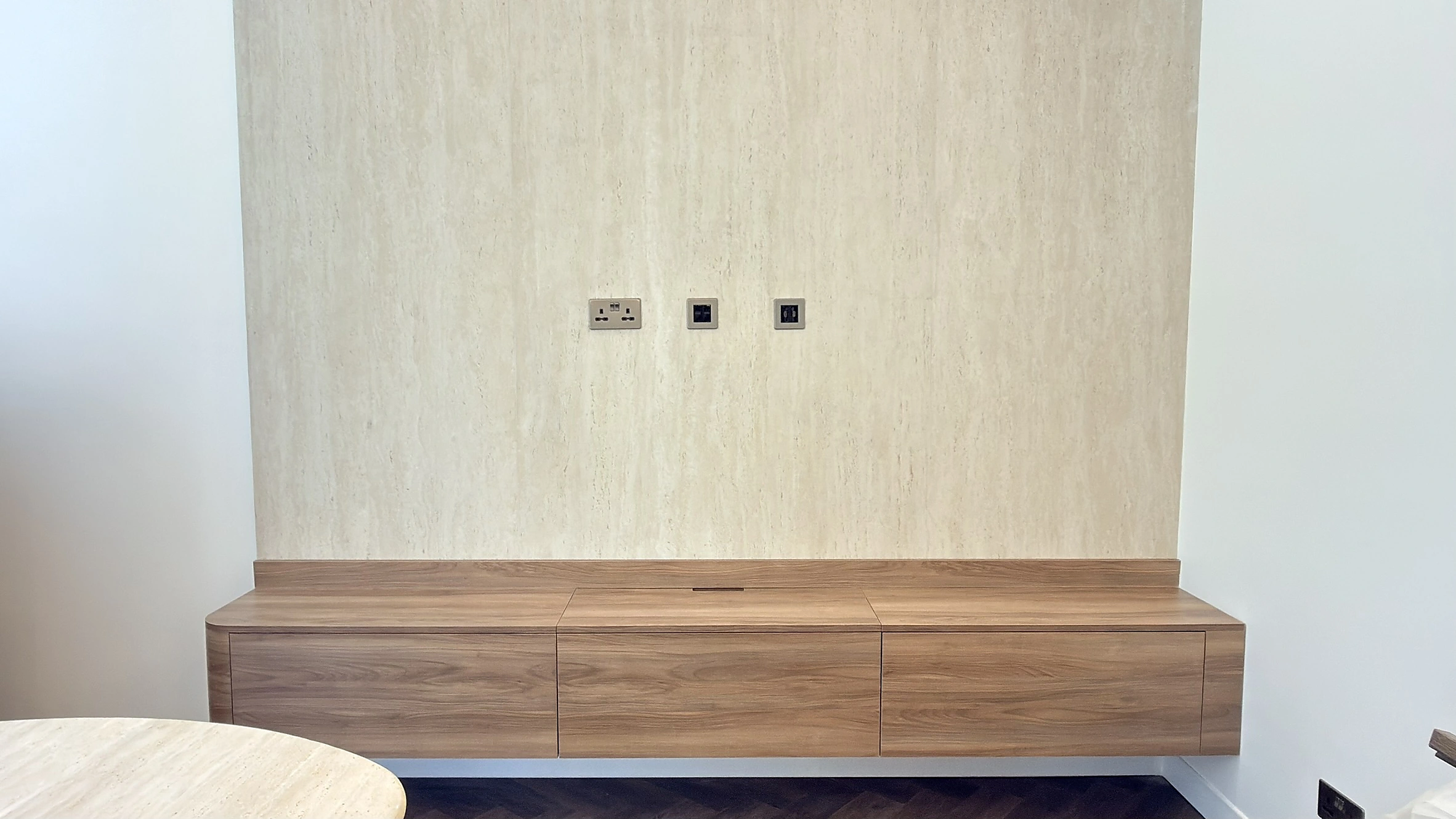 Floating walnut dining sideboard against a travertine wall, Dubai