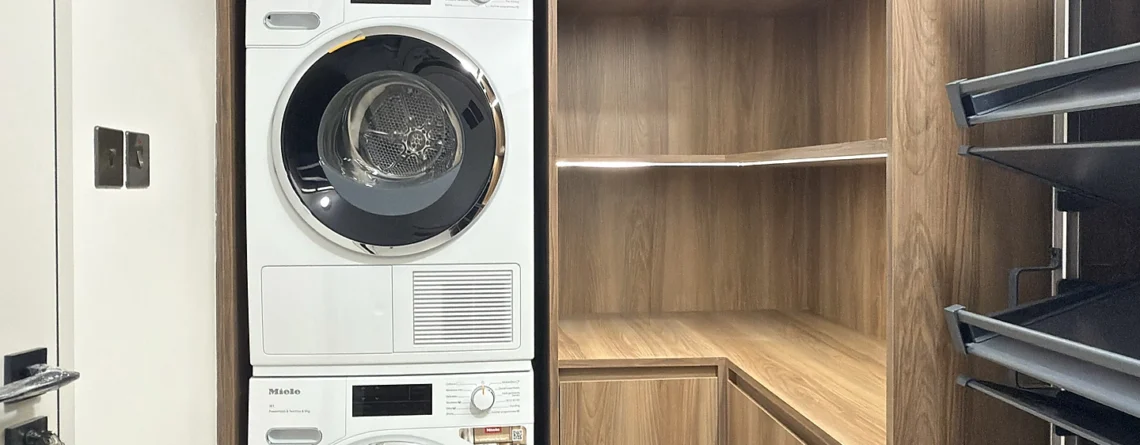 Laundry room fit-out in Dubai with walnut Egger cabinetry, stacked appliances and pull-out racks